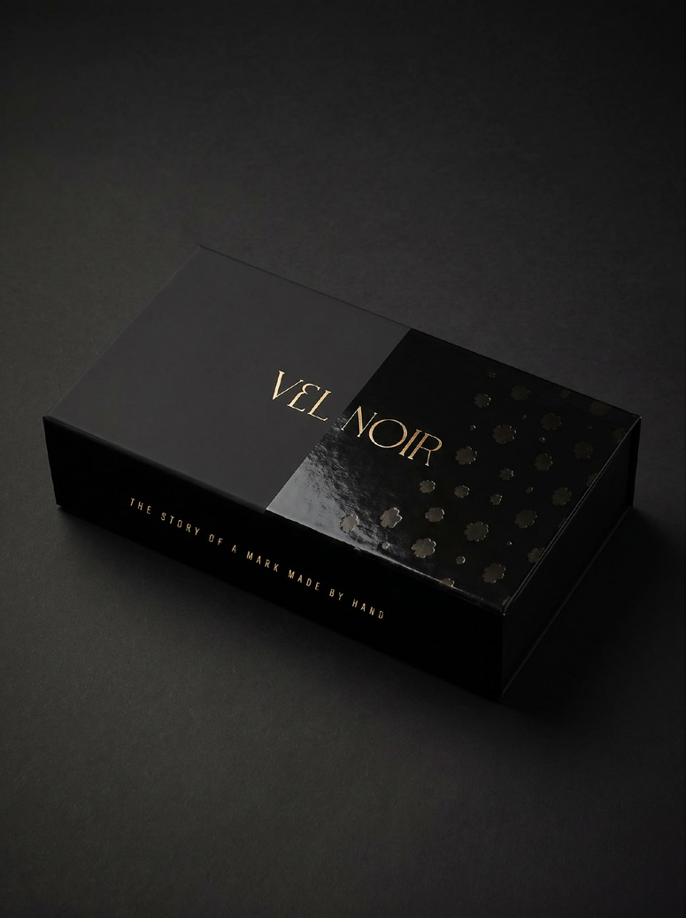 Vel Noir luxury packaging — matte black presentation box with gold foil wordmark and gloss pattern detail